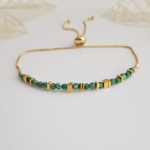 Puede incluir: Una pulsera ajustable dorada con peque&ntilde;as cuentas verdes redondas e incrustaciones rectangulares doradas. La pulsera tiene una cadena delicada y un cierre de cuentas deslizantes.