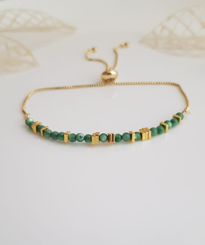 Puede incluir: Una pulsera ajustable dorada con peque&ntilde;as cuentas verdes redondas e incrustaciones rectangulares doradas. La pulsera tiene una cadena delicada y un cierre de cuentas deslizantes.