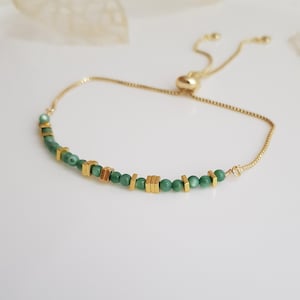 Puede incluir: Pulsera ajustable dorada con peque&ntilde;as cuentas verdes redondas y cuentas cuadradas doradas. La pulsera tiene una cadena delicada y un cierre deslizante. Adecuada para mu&ntilde;ecas de hasta 20 cm.