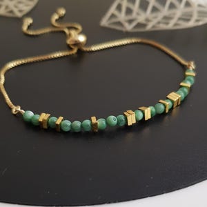 Puede incluir: Pulsera dorada con una cadena delicada y un cierre deslizante para ajustar la talla. La pulsera est&aacute; adornada con peque&ntilde;as cuentas verdes redondas y detalles rectangulares dorados. El dise&ntilde;o es sencillo pero elegante, adecuado para el uso diario.