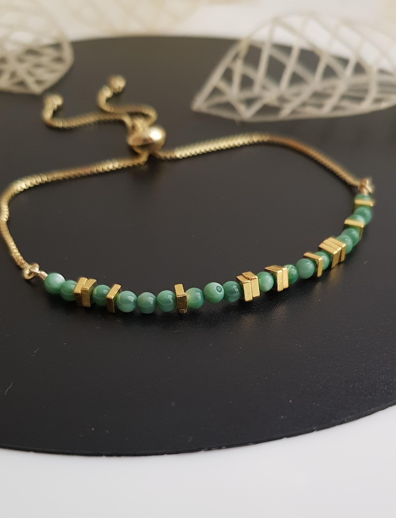 Puede incluir: Pulsera dorada con una cadena delicada y un cierre deslizante para ajustar la talla. La pulsera est&aacute; adornada con peque&ntilde;as cuentas verdes redondas y detalles rectangulares dorados. El dise&ntilde;o es sencillo pero elegante, adecuado para el uso diario.