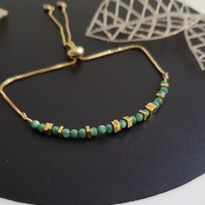 Puede incluir: Pulsera dorada con una delicada cadena y una fila de cuentas verdes intercaladas con detalles geom&eacute;tricos dorados. La pulsera ajustable tiene un cierre deslizante. Una elegante pieza de joyer&iacute;a.