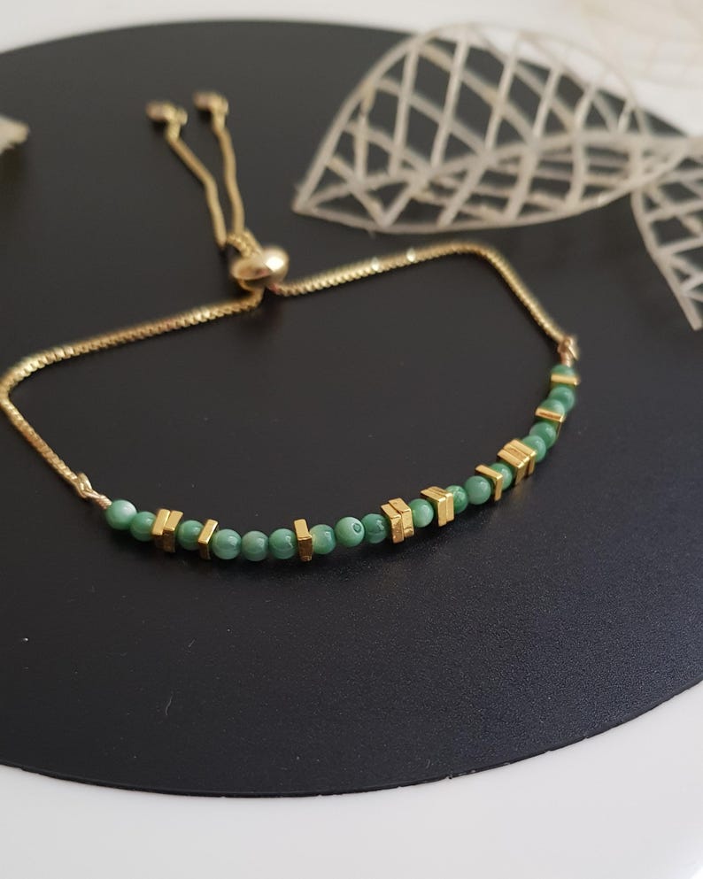 Puede incluir: Pulsera dorada con una delicada cadena y una fila de cuentas verdes intercaladas con detalles geom&eacute;tricos dorados. La pulsera ajustable tiene un cierre deslizante. Una elegante pieza de joyer&iacute;a.