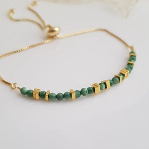 Puede incluir: Pulsera ajustable dorada con peque&ntilde;as cuentas verdes redondas y cuentas cuadradas doradas. La pulsera tiene una cadena delicada y un cierre deslizante. Mide aproximadamente 18 cm de largo.