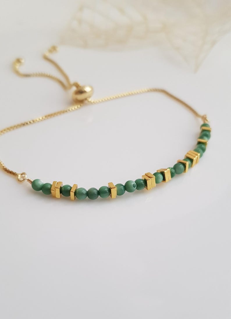 Puede incluir: Pulsera ajustable dorada con peque&ntilde;as cuentas verdes redondas y cuentas cuadradas doradas. La pulsera tiene una cadena delicada y un cierre deslizante. Mide aproximadamente 18 cm de largo.