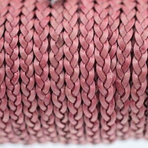 May include: A spool of dusty rose coloured braided cord featuring a tight, uniform weave pattern. The cord is composed of multiple strands intertwined to create a continuous, textured rope-like structure with a matte finish throughout the length.