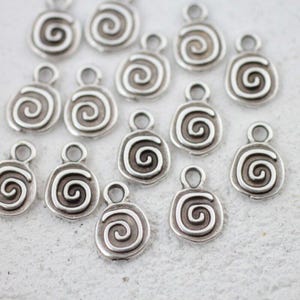 以下が含まれることがあります： 小さな銀色の渦巻きチャームのコレクション。各チャームは、中央に渦巻き模様があり、上部に小さなループが付いた丸みを帯びた長方形の形をしており、ジュエリーやその他の工芸品に取り付けることができます。