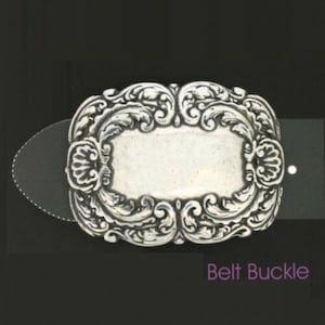 Puede incluir: Hebilla de cinturón plateada con un diseño ornamental de volutas. La hebilla rectangular tiene un área central en blanco y está sujeta a una correa negra. Las palabras "Belt Buckle" están en la esquina inferior derecha.