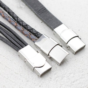 May include: Close-up of three leather bracelets with silver-colored magnetic clasps. One bracelet is black, another is braided black and brown, and the third is gray. The bracelets are displayed on a light-colored surface.