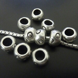 May include: Silver-toned metal beads with a textured surface and large central holes. Some beads are round, others are cylindrical, and all are strung on a silver chain. The beads have a slightly aged appearance.