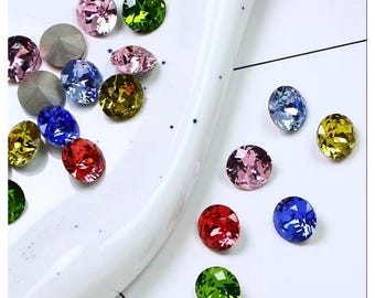 May include: An assortment of colorful, faceted gemstones in various shapes and sizes. The gems are in shades of pink, green, yellow, blue, and red. Some are round, while others are oval. The gems are scattered on a white surface.