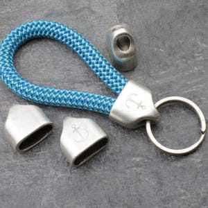 May include: A blue and white rope keychain with silver-colored metal accents. The keychain features an anchor emblem and a split ring for keys. Several metal pieces are also included.