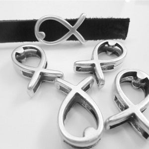 May include: Silver-toned metal charms in a fish symbol design. One charm is attached to a black suede band, while four others are scattered nearby. The charms have a detailed, openwork design, and the background is a bright white.