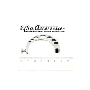 Puede incluir: Un hallazgo de joyería plateado y curvado con una serie de agujeros circulares y ovalados. La pieza tiene un extremo cuadrado y un pequeño pomo redondo. Una regla muestra las medidas en centímetros. El texto "EfSa Accessoires" es visible.