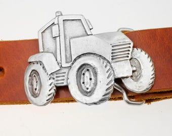 Op de afbeelding: Zilverkleurige tractorriemgesp bevestigd aan een bruine leren riem. De tractor heeft grote banden en gedetailleerde kenmerken. De gesp is een accessoire met boerderijthema.