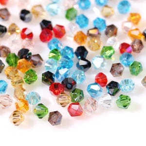 May include: A collection of multi-coloured faceted beads, including red, blue, green, and amber. The beads are scattered on a white surface, highlighting their many facets and light-reflecting properties. Suitable for jewellery making or craft projects.