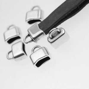 May include: Several silver-coloured metal cord end caps with a loop, designed to secure and finish the ends of cords or straps. A black leather strap is also visible. The caps are small, rectangular, and have a shiny finish, suitable for jewellery making or crafts.