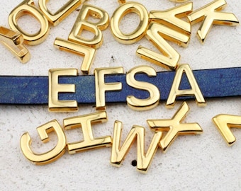 May include: Gold-colored metal alphabet letters scattered around a blue leather strap. The letters are in various fonts and sizes, with some letters arranged to spell out "EFSA". The letters are shiny and reflect light.