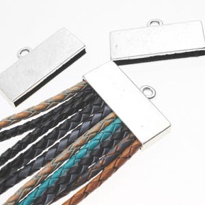 May include: A multi-strand leather bracelet with a silver magnetic clasp. The braided leather strands are in shades of brown, black, and teal. The clasp has a small loop for attaching to other jewellery components.