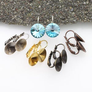 May include: An assortment of earring components in various metallic finishes, including silver, gold, and bronze. The selection features lever-back closures and round, flat, and faceted crystal designs. The earrings are displayed on a white surface.