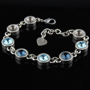 May include: Silver-toned bracelet featuring oval and round light blue gemstones. The bracelet has a chain link design with a heart-shaped charm near the clasp. The gemstones are set in individual silver bezels.