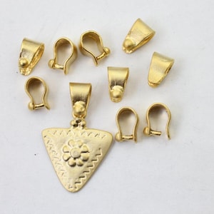 Könnte beinhalten: Eine Sammlung goldfarbener Schmuckzubehörteile, darunter Anhängerbügel und ein dreieckiger Anhänger. Der Anhänger hat ein Blumenmuster und Zickzackkanten. Die Bügel haben ein Schlaufendesign mit einer kleinen Kugel an der Basis.