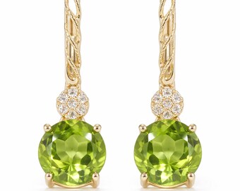 May include: A pair of gold-coloured drop earrings. Each earring features a light green, oval-shaped gemstone suspended from a gold-coloured hoop with a textured design. Small, clear gemstones are set above the green stone.