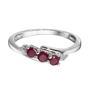 May include: A silver ring with three round, deep red gemstones. The ring has a curved design with the gemstones clustered together. Small, clear stones are set on either side of the red gemstones.