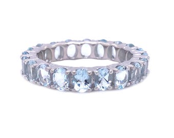 May include: A silver eternity ring featuring a continuous row of oval-cut, light blue gemstones. The ring's band is made of polished silver, and the gemstones are evenly spaced around the entire circumference.