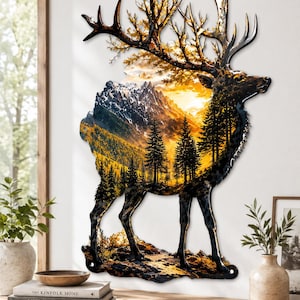 Könnte beinhalten: Ein Wandkunstobjekt aus Metall in Form einer Hirschsilhouette mit einem detaillierten Landschaftsdruck von schneebedeckten Bergen, einem goldenen Sonnenuntergang und einem dichten Kiefernwald. Das Kunstwerk hat einen dunklen Metallrand.
