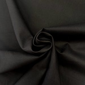 May include: A close-up of a tightly curled swatch of black fabric, showcasing its texture and drape. The fabric is a solid colour, with a subtle sheen. The image highlights the fabric's smooth surface and the way it folds and gathers.