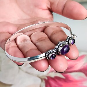 Op de afbeelding: Een zilveren armband met drie paarse edelstenen. De armband heeft een decoratief ontwerp met kleine zilveren kralen rond de edelstenen. De tekst "ihbjewel" is zichtbaar.