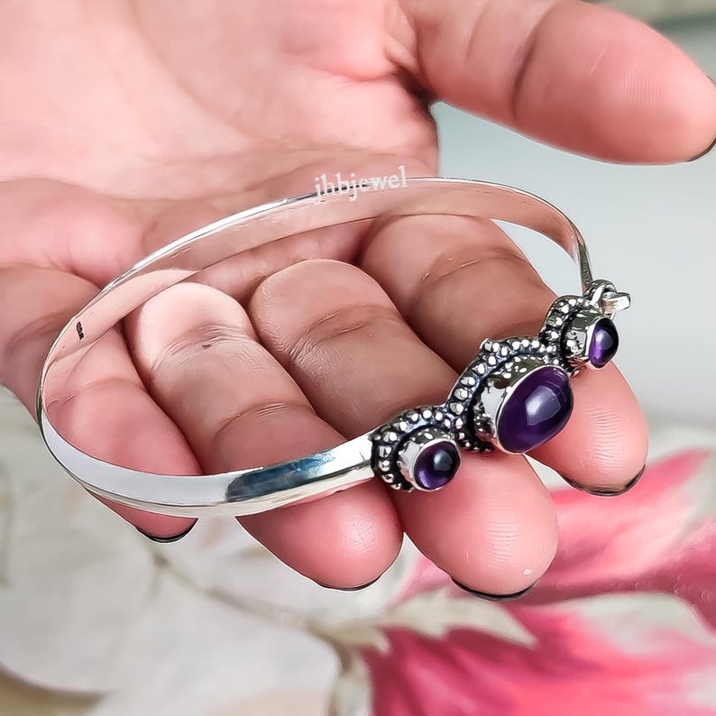 Op de afbeelding: Een zilveren armband met drie paarse edelstenen. De armband heeft een decoratief ontwerp met kleine zilveren kralen rond de edelstenen. De tekst "ihbjewel" is zichtbaar.