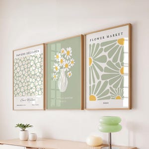 Può includere: Tre stampe artistiche floreali incorniciate. Le stampe presentano disegni di margherite e fiori nei toni del bianco, giallo e verde. Il testo sulle stampe include "PAPIERS DÉCOUPÉS", "LA MAISON BOHÈME PARIS" e "FLOWER MARKET PARIS".