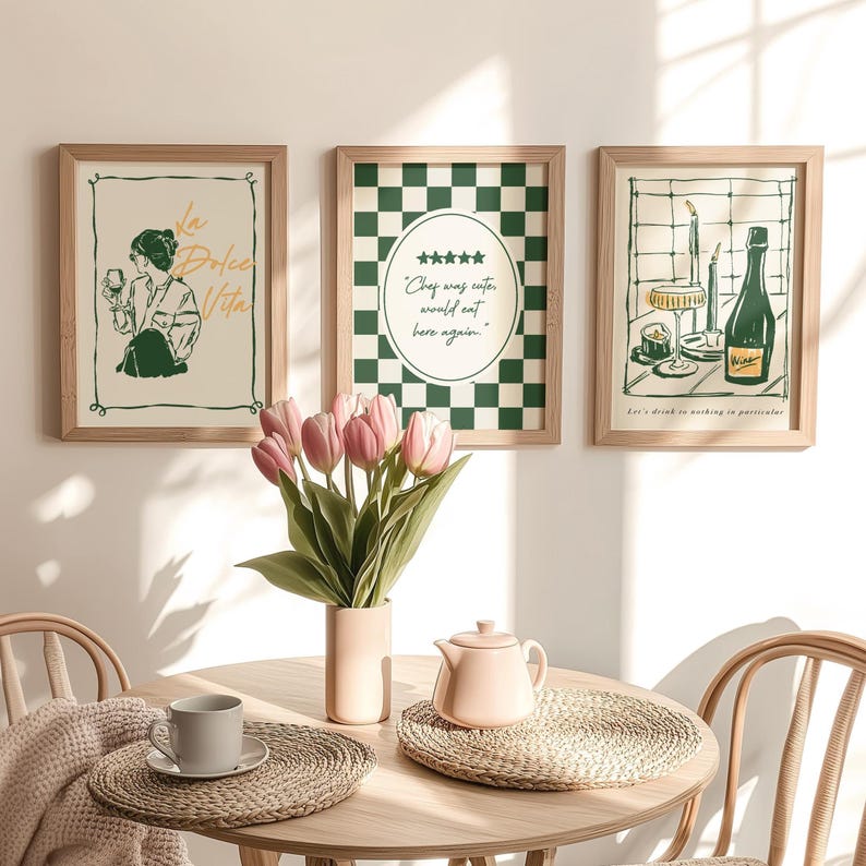 May include: Three framed art prints with wooden frames are displayed above a table. The prints feature illustrations and text, including "La Dolce Vita" and "Chef was cuter would eat here again." A vase of pink tulips and a tea set are on the table.