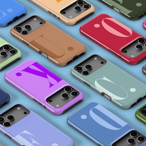 May include: A collection of brightly coloured phone cases in shades like blue, green, pink, and brown. Each case has a unique design, some with a letter or shape. The cases are arranged on a light blue surface.