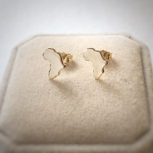 Puede incluir: Un par de pendientes de oro con forma del continente africano. Los pendientes son pequeños y delicados, y serían un gran regalo para alguien que ama África.
