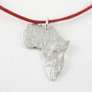 Può includere: Una collana d'argento con un ciondolo a forma del continente africano. Il ciondolo ha un'apertura a forma di cuore al centro.