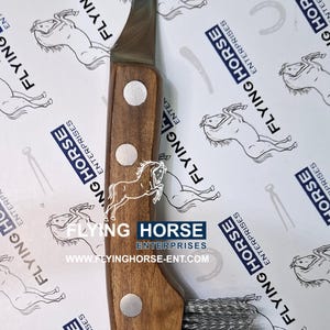 Puede incluir: Un cuchillo para cascos con mango de madera y hoja curva. El cuchillo tiene un cepillo de metal en el extremo y está diseñado para recortar cascos de caballos. El fondo presenta el logotipo de Flying Horse Enterprises.