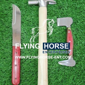 Puede incluir: Tres herramientas de herrador sobre una superficie verde. Un cuchillo para cascos con mango de madera rojo, un martillo con mango de madera clara y una tenaza para cascos con mango de madera rojo. El texto "FLYING HORSE ENTERPRISES" es visible.