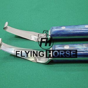 May include: Two stainless steel hoof knives with blue and white patterned handles. The blades are curved and sharp, designed for trimming horse hooves. The logo "FLYING HORSE" is visible.
