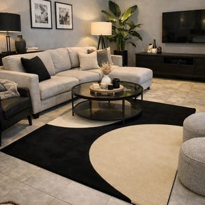 May include: A modern living room featuring a large sectional sofa, a round glass coffee table, and a black and beige geometric rug. The room is decorated with neutral tones, black lamps, and framed artwork, creating a stylish and comfortable space.