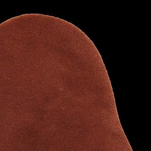 May include: Close-up of a section of a brown, textured fabric. The material has a soft, plush appearance, with a slightly curved edge against a black background. The color is a warm, earthy tone, suggesting a cozy textile.