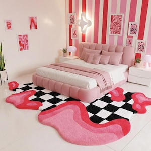 Könnte beinhalten: Ein rosa Schlafzimmer mit Bett, Kissen und Teppich. Das Bett hat ein rosa Kopfteil und ist mit einer weißen Bettdecke und einer rosa Decke bedeckt. Der Teppich ist schwarz-weiß kariert mit rosa und roten Formen.