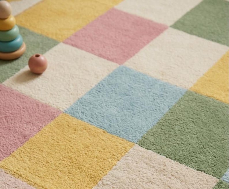 Soft pastel checkerboard nursery rug with scalloped border in pink, sage green, cream, yellow, and baby blue, styled in a cozy rainbow-themed kids room with plush tufted texture.