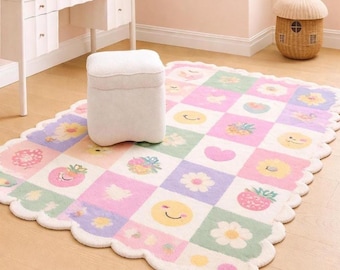 Puede incluir: Una alfombra rectangular con borde festoneado que presenta un patrón de cuadrícula con cuadrados en tonos pastel rosa, morado, verde y amarillo. Los cuadrados contienen varios iconos gráficos, incluyendo soles sonrientes, flores, fresas y corazones.