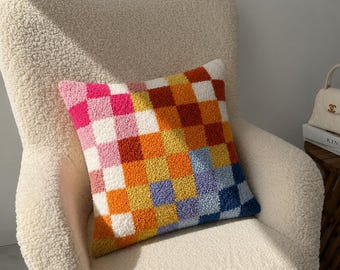 Pode incluir: Uma almofada quadrada com acabamento em tufting apresentando um padrão vibrante de xadrez. O design consiste em pequenos quadrados texturizados em tons de rosa choque, rosa claro, branco, amarelo, laranja, vermelho ferrugem, lavanda e azul.