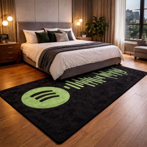 Pode incluir: Um tapete retangular preto com o logotipo verde do Spotify e um design de onda sonora. O tapete está colocado em um piso de madeira em frente a uma cama com roupa de cama branca e travesseiros cinza. O quarto tem uma estética moderna.