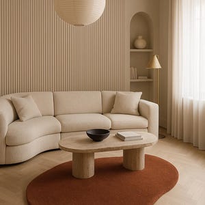 May include: A modern living room with a beige sectional sofa, a stone coffee table, and a rust-colored, organic-shaped rug. A paper lantern hangs from the ceiling, and a gold floor lamp stands near a window with sheer curtains. The walls are a neutral beige.