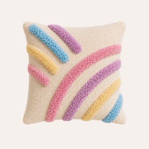 Pode incluir: Uma almofada quadrada com uma base de cor creme apresentando uma textura tufada. A superf&iacute;cie &eacute; decorada com linhas diagonais em relevo em tons pastel de azul claro, amarelo, rosa e lavanda, criando um padr&atilde;o suave e multicolorido.